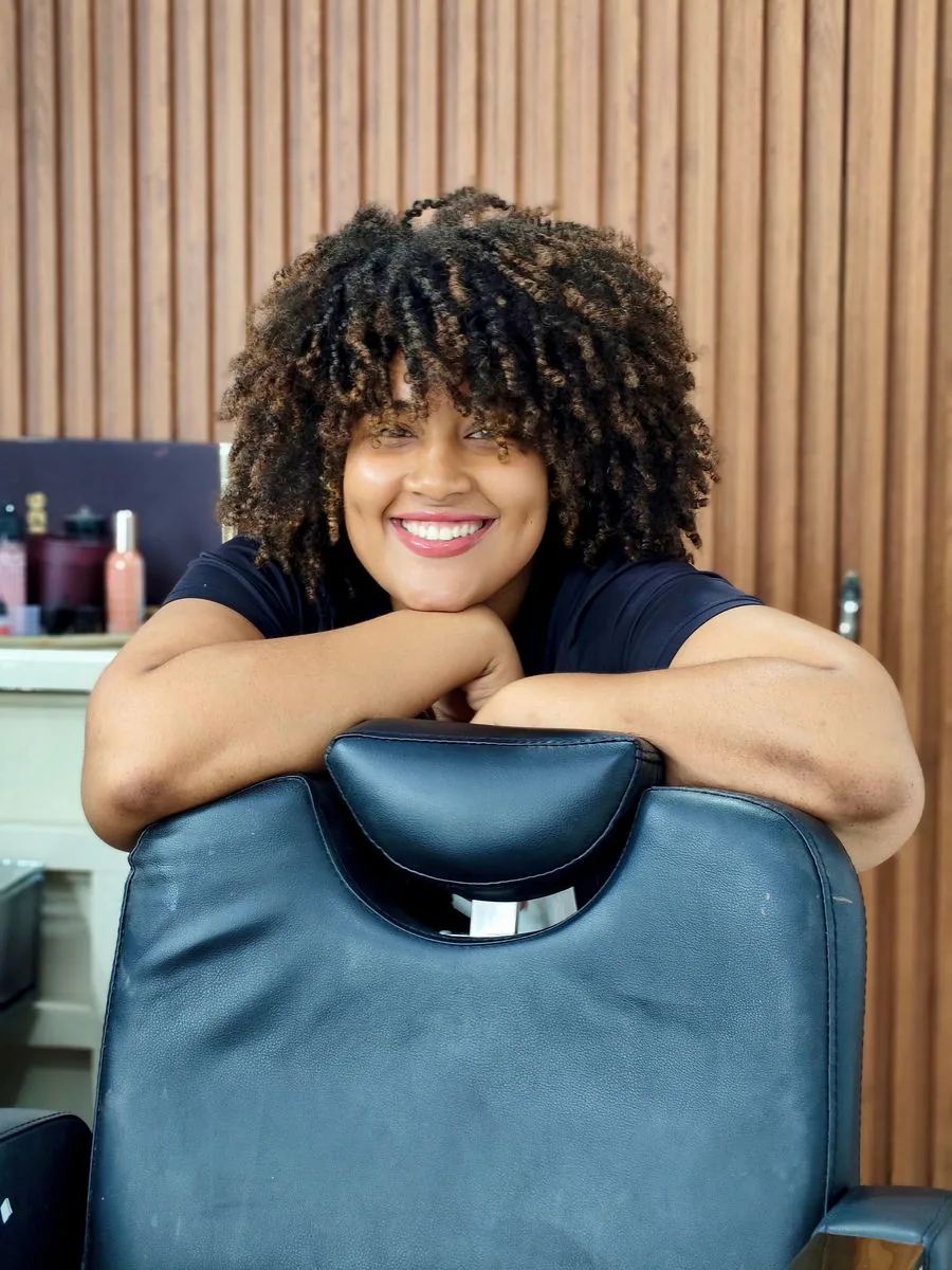 A smiling stylist leaning on her own salon chair